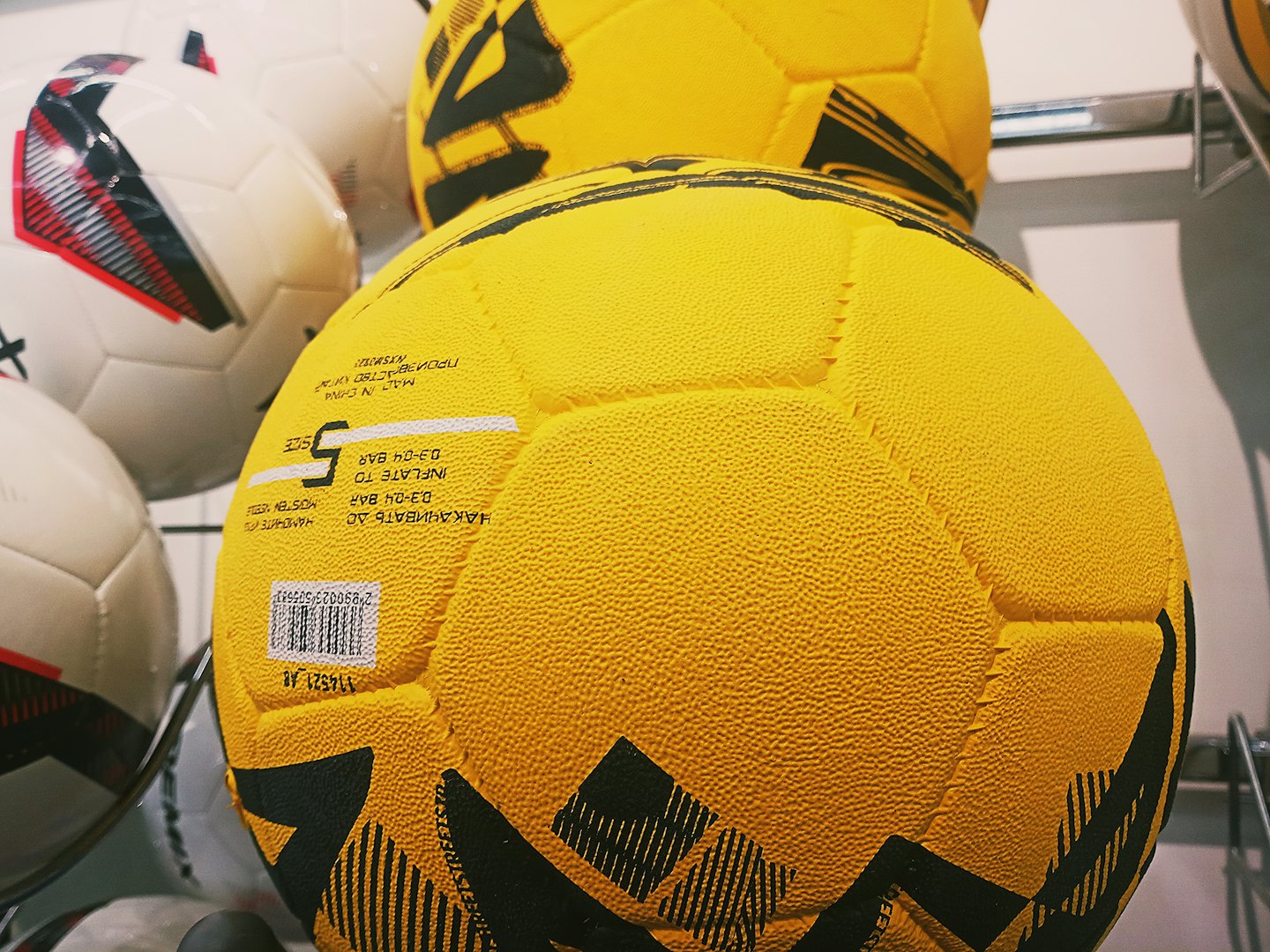 Palloni da calcio gialli e bianchi esposti su uno scaffale da negozio.