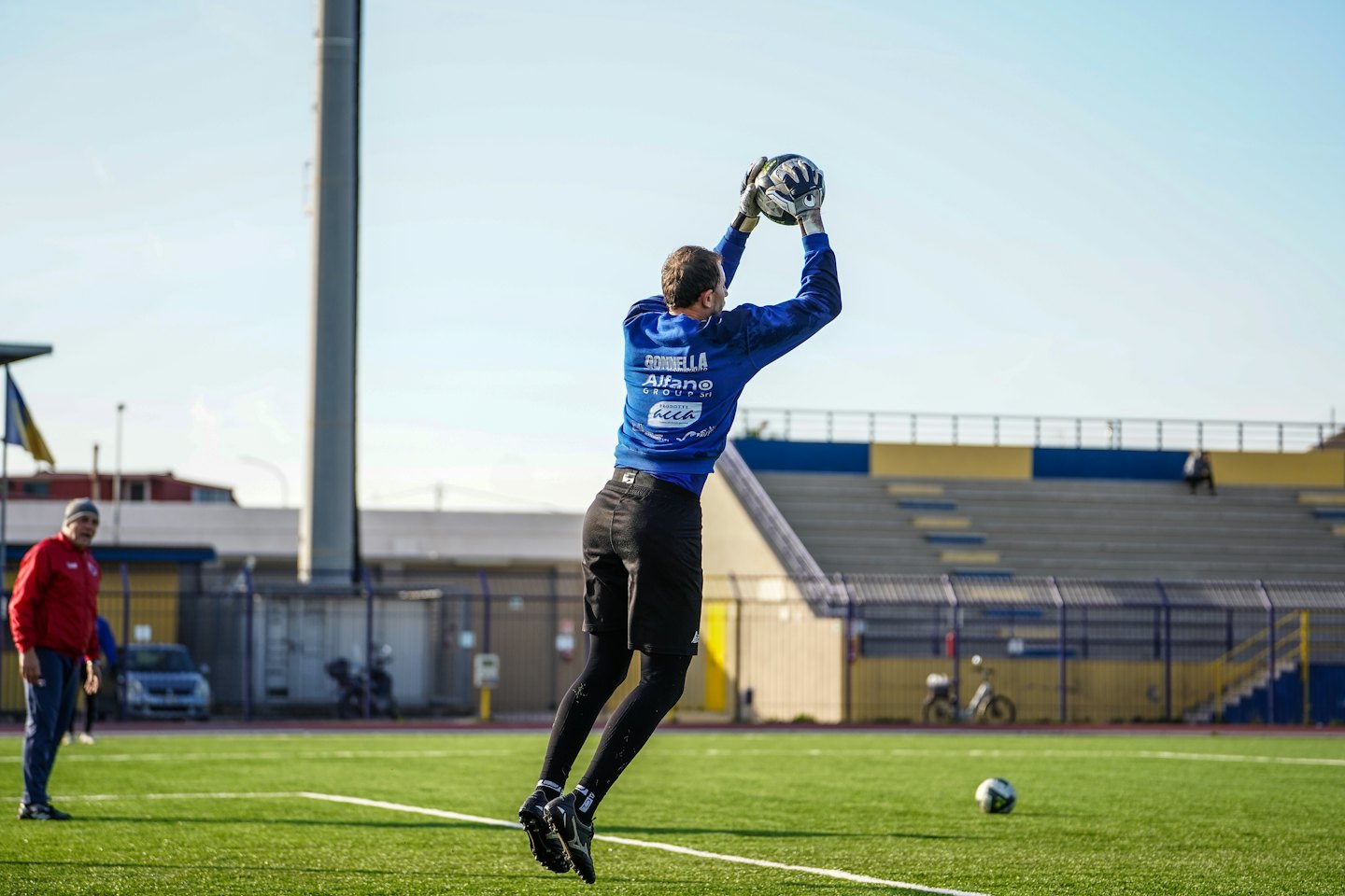 Portiere in maglia blu salta per afferrare un pallone da calcio.